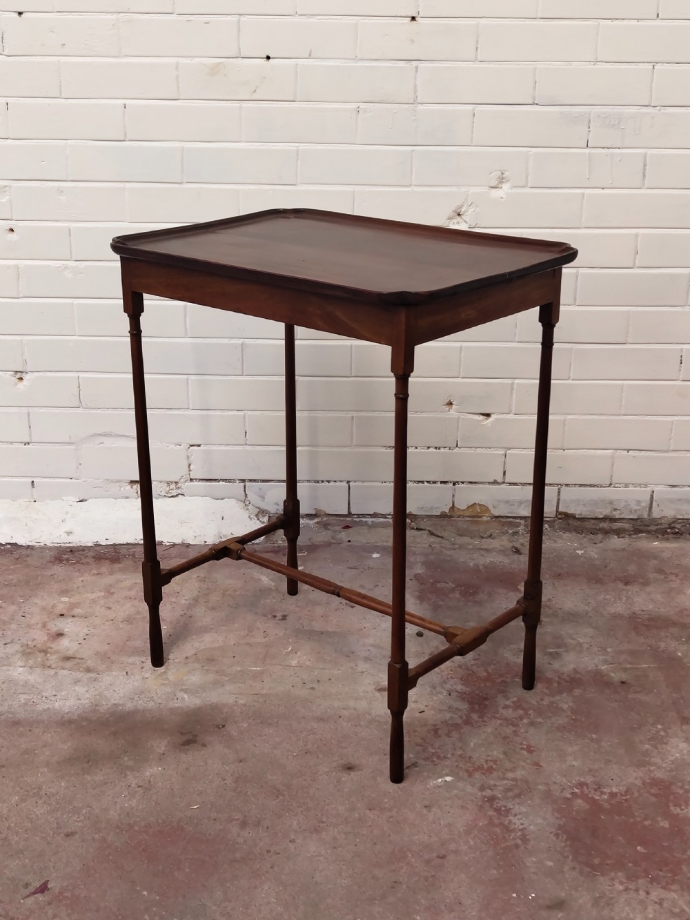 A tall Edwardian mahogany occasional table featuring a tray top with raised edges and slender spider legs connected by lower stretchers. View II