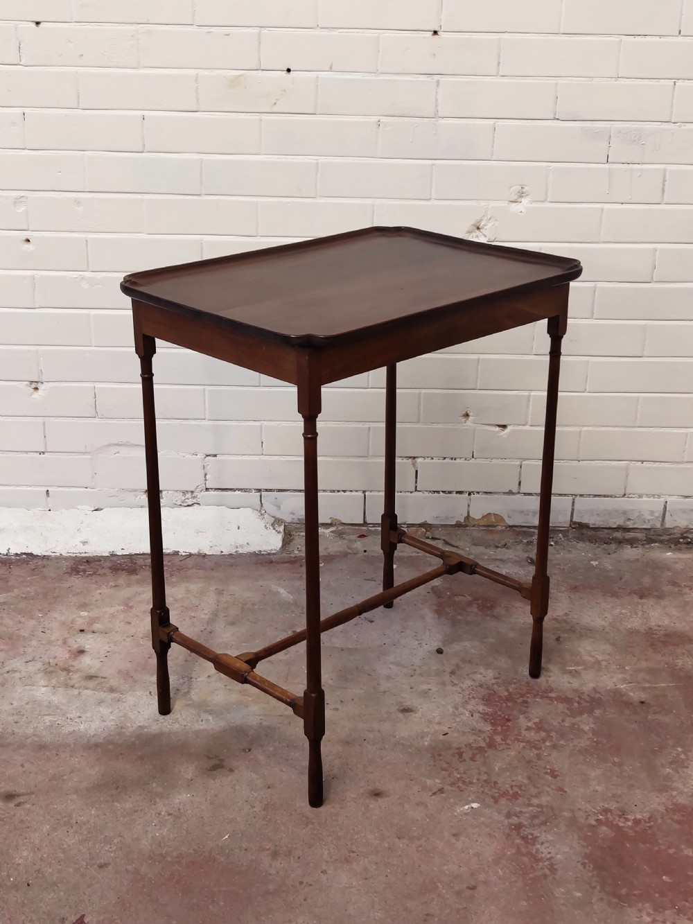 A tall Edwardian mahogany occasional table featuring a tray top with raised edges and slender spider legs connected by lower stretchers.