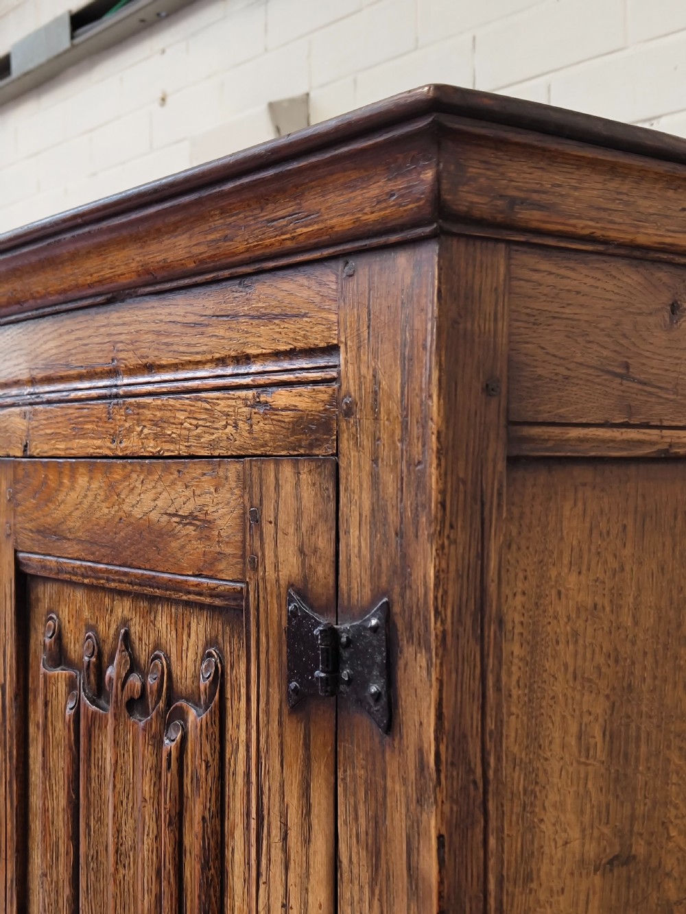 A tall solid oak double wardrobe featuring carved linenfold upper panels and black iron strap hinges. View II
