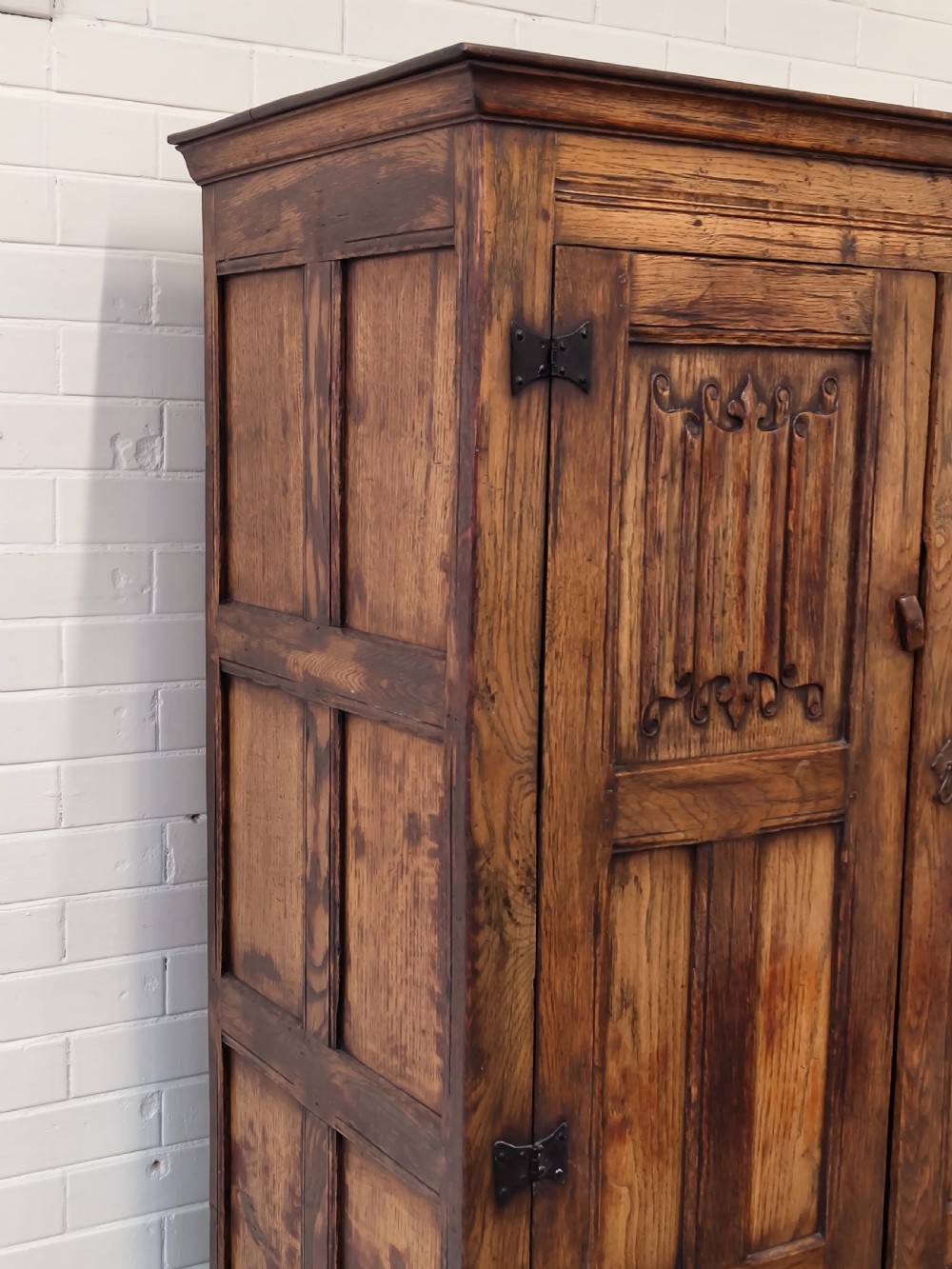 A tall solid oak double wardrobe featuring carved linenfold upper panels and black iron strap hinges. View VI