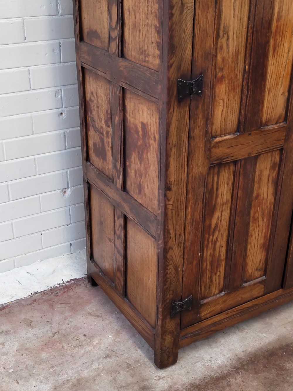 A tall solid oak double wardrobe featuring carved linenfold upper panels and black iron strap hinges. View VII