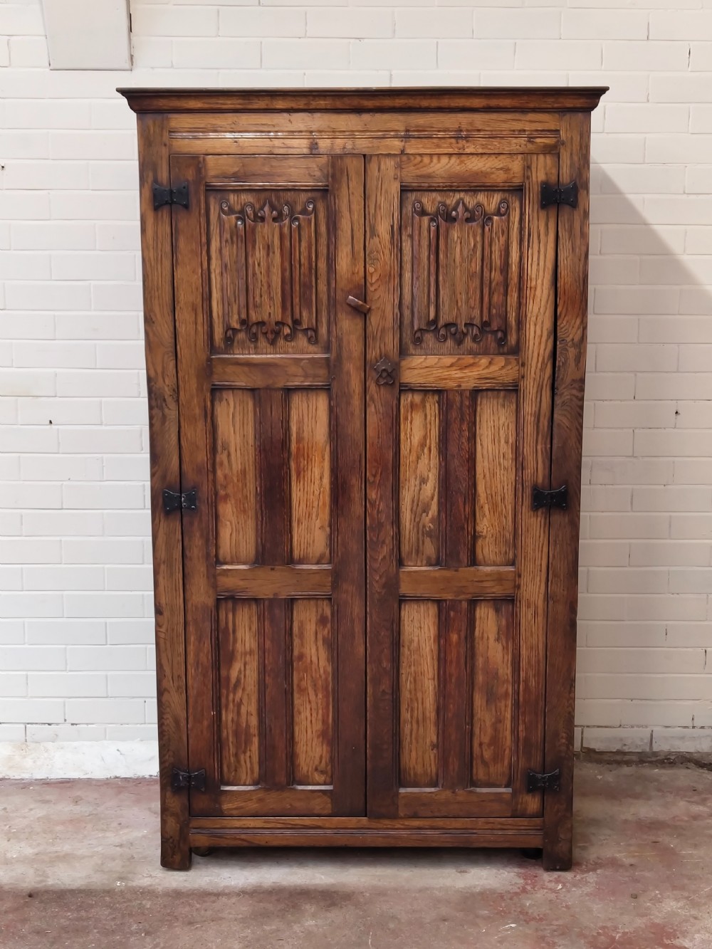 A tall solid oak double wardrobe featuring carved linenfold upper panels and black iron strap hinges. View VIII