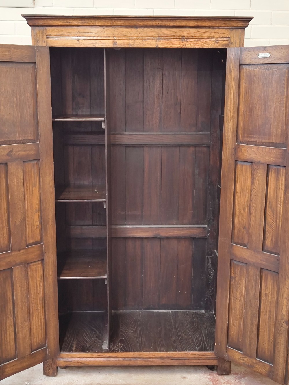 A tall solid oak double wardrobe featuring carved linenfold upper panels and black iron strap hinges. View XI