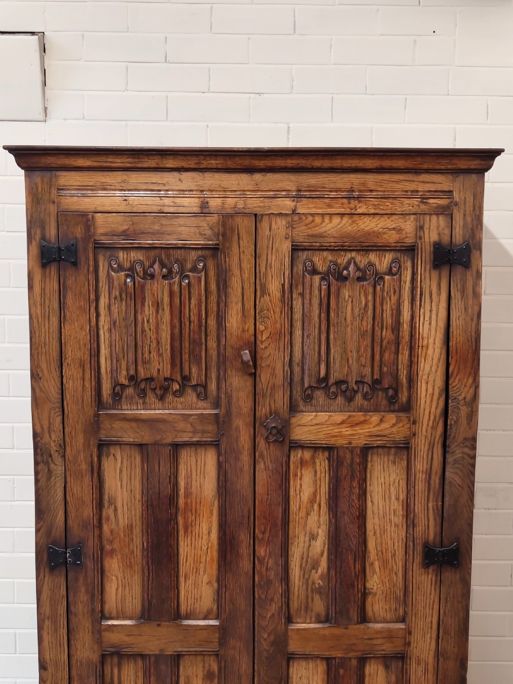 A tall solid oak double wardrobe featuring carved linenfold upper panels and black iron strap hinges. View XIII