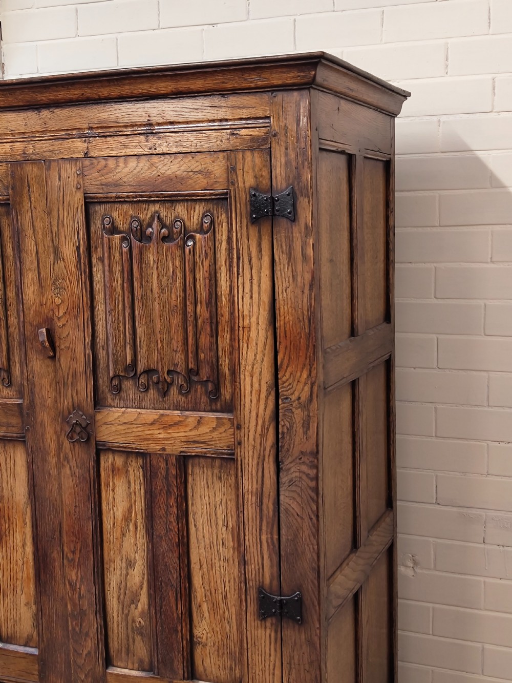 A tall solid oak double wardrobe featuring carved linenfold upper panels and black iron strap hinges. View XIV