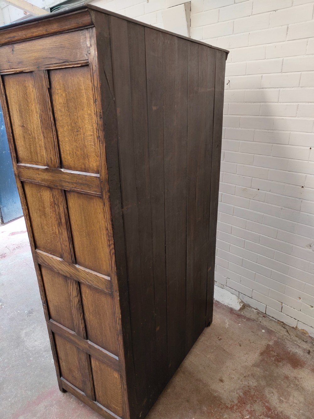 A tall solid oak double wardrobe featuring carved linenfold upper panels and black iron strap hinges. View XV
