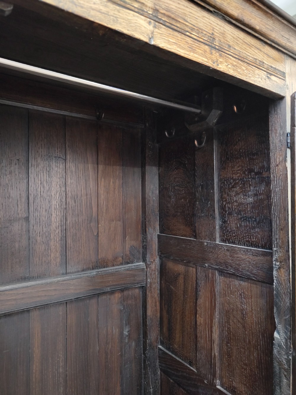 A tall solid oak double wardrobe featuring carved linenfold upper panels and black iron strap hinges. View XVI