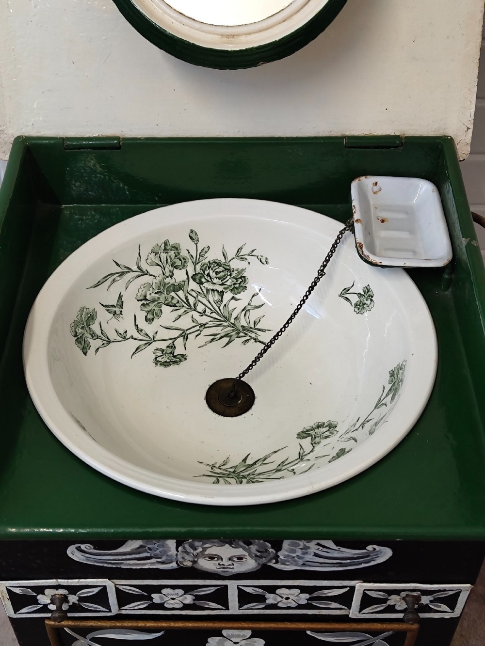 A hand-painted black and green metal toleware washstand with an open lid revealing a circular mirror and a fitted ceramic washbasin. View XVII