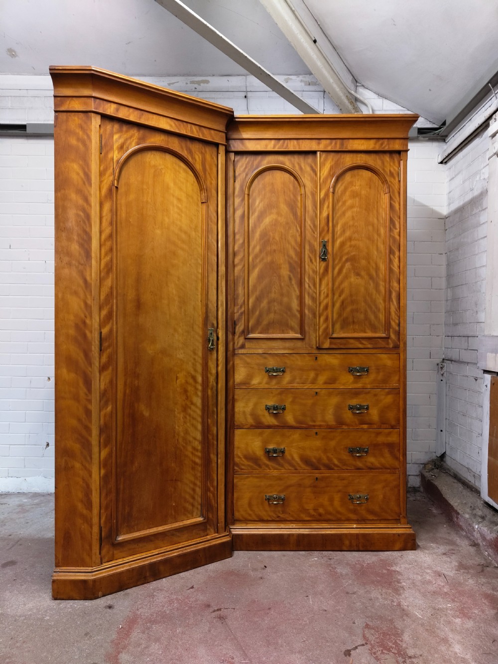 Victorian satin birch corner compactum wardrobe featuring arched panelled doors, brass hardware, and a integrated chest of drawers.