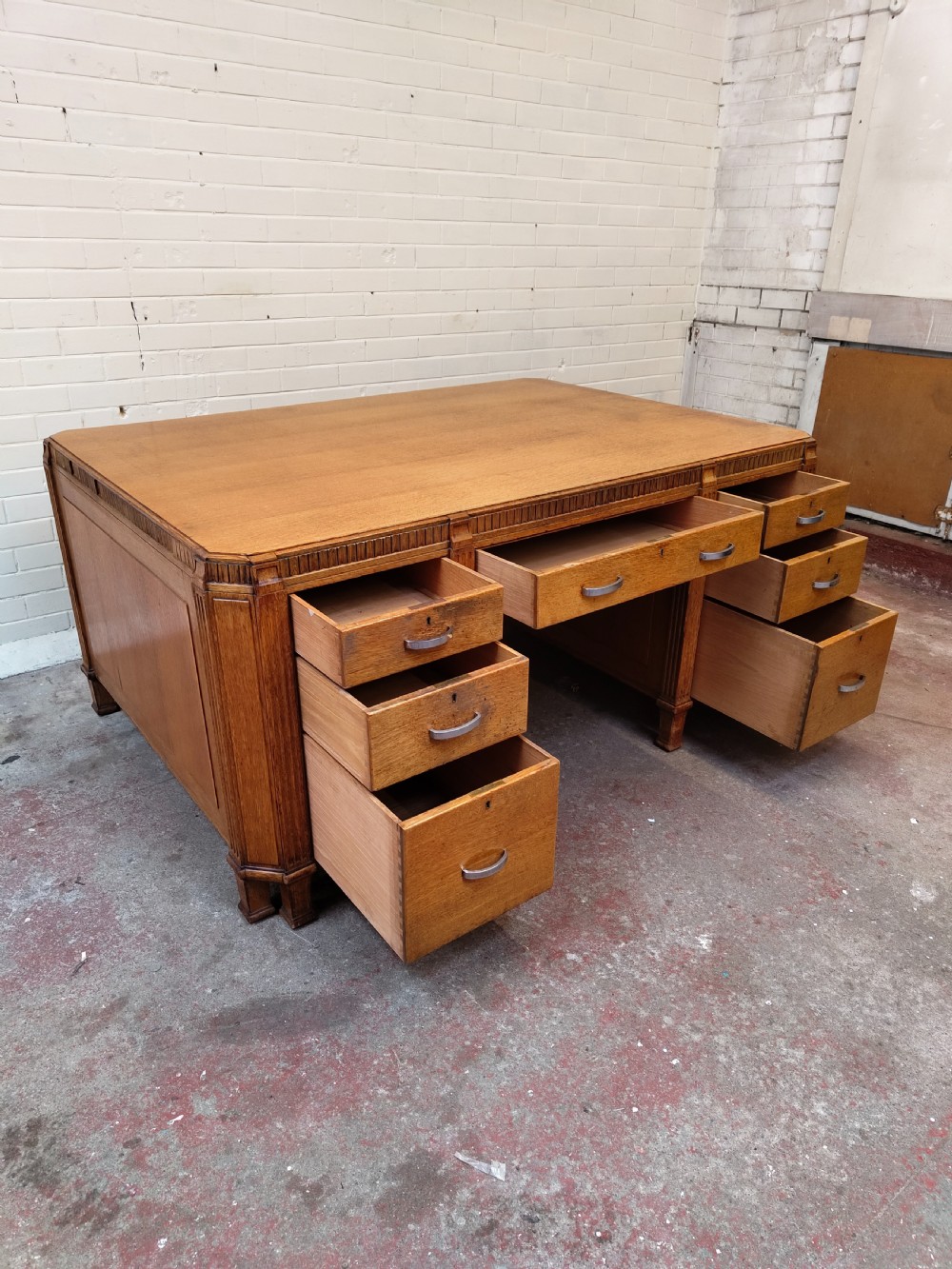 A large golden oak Art Deco partners desk featuring reeded corner details, dual pedestals with drawers, and metal pull handles. View IX