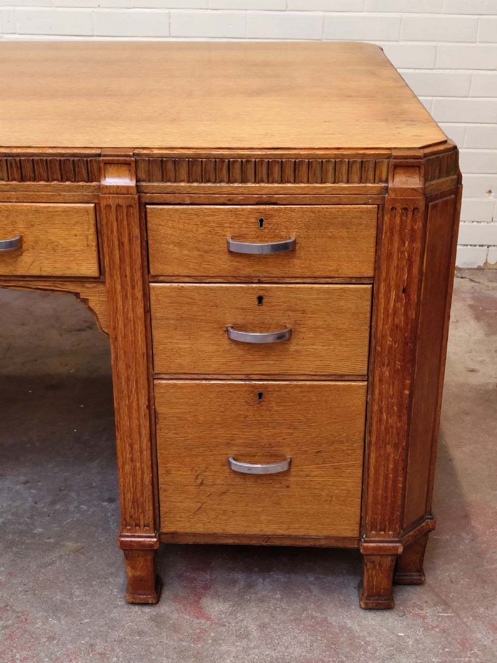 A large golden oak Art Deco partners desk featuring reeded corner details, dual pedestals with drawers, and metal pull handles. View VI