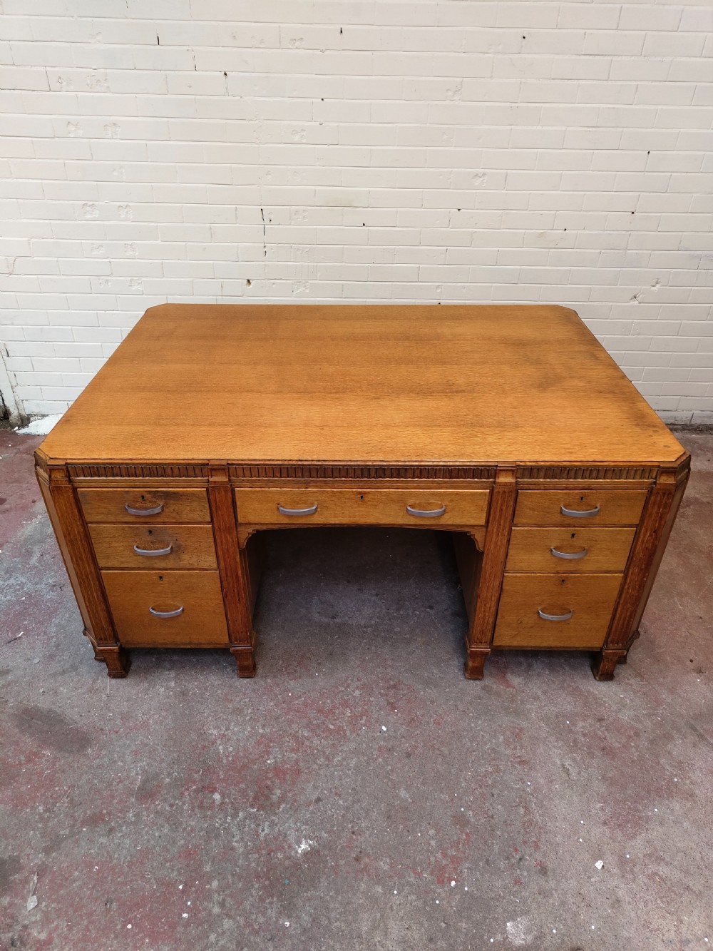 A large golden oak Art Deco partners desk featuring reeded corner details, dual pedestals with drawers, and metal pull handles. View VII