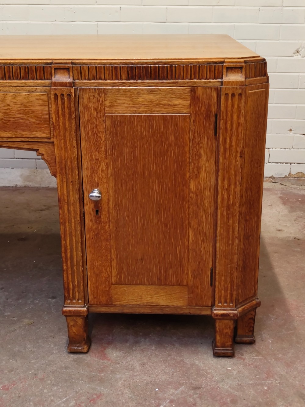 A large golden oak Art Deco partners desk featuring reeded corner details, dual pedestals with drawers, and metal pull handles. View X