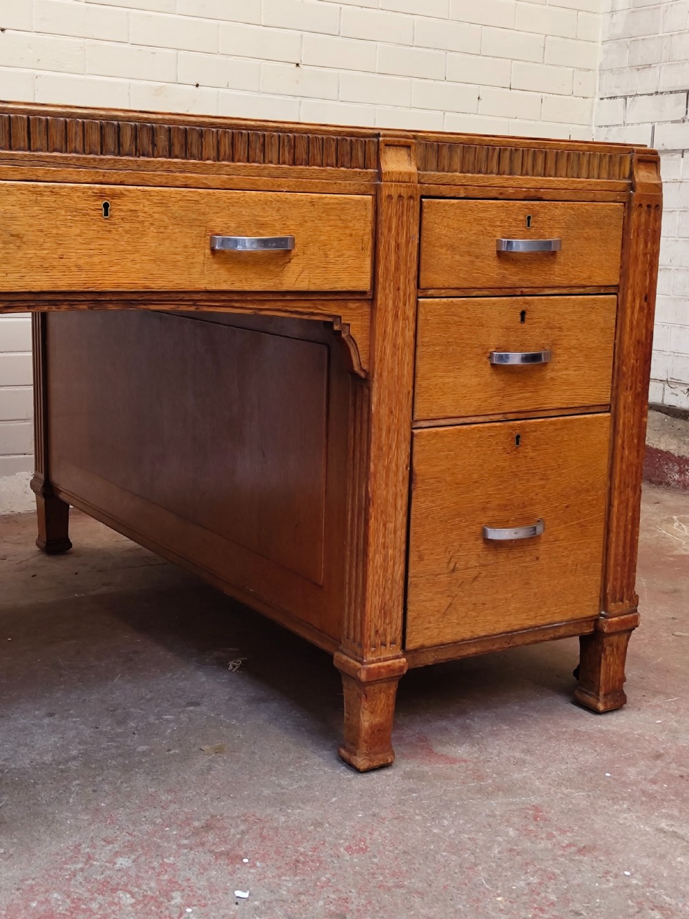 A large golden oak Art Deco partners desk featuring reeded corner details, dual pedestals with drawers, and metal pull handles. View XI