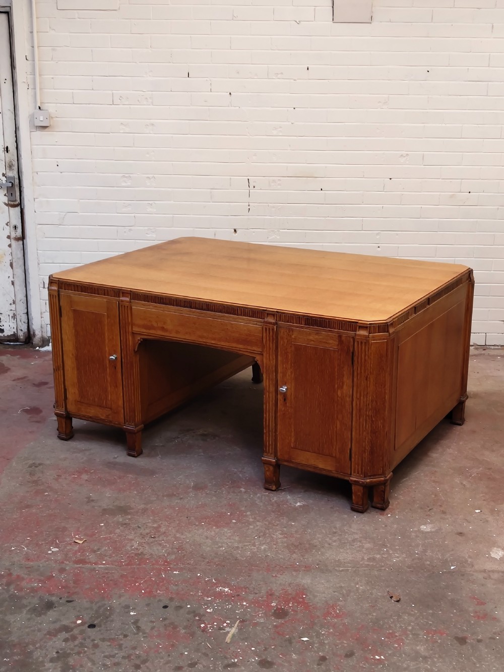 A large golden oak Art Deco partners desk featuring reeded corner details, dual pedestals with drawers, and metal pull handles. View XII