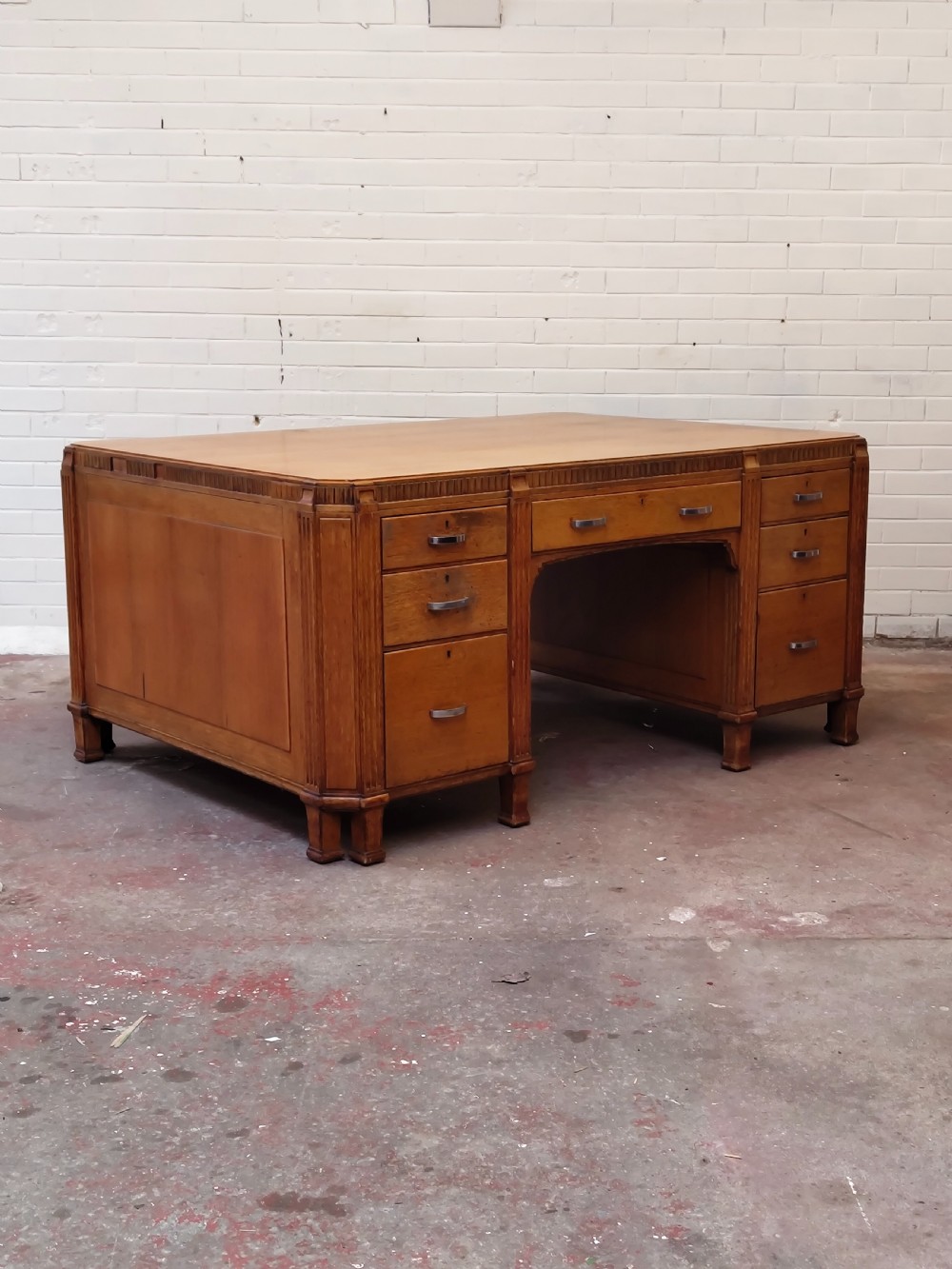 A large golden oak Art Deco partners desk featuring reeded corner details, dual pedestals with drawers, and metal pull handles. View XV