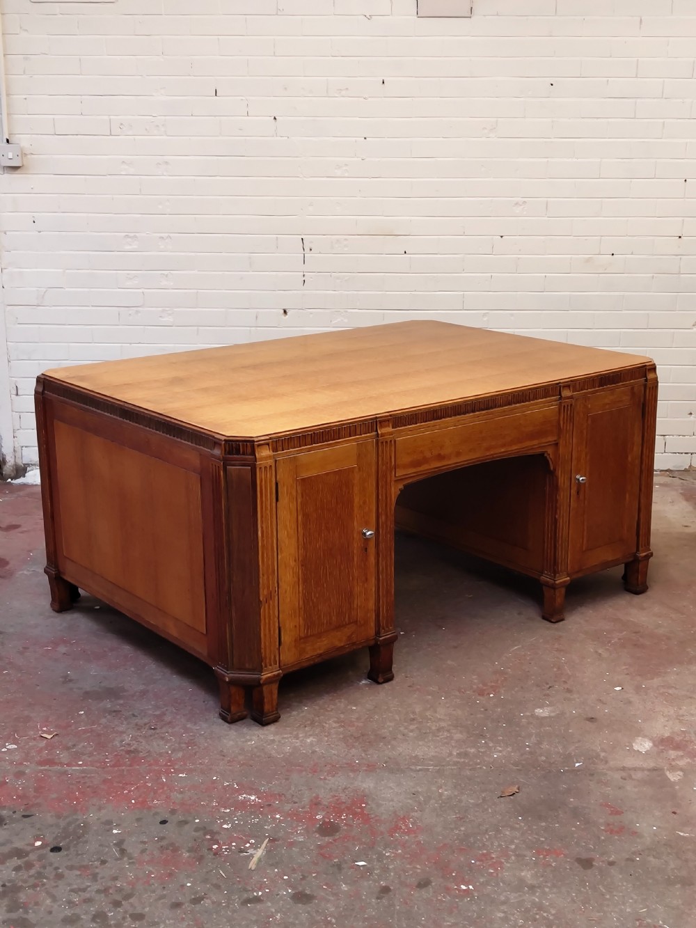 A large golden oak Art Deco partners desk featuring reeded corner details, dual pedestals with drawers, and metal pull handles. View XVII