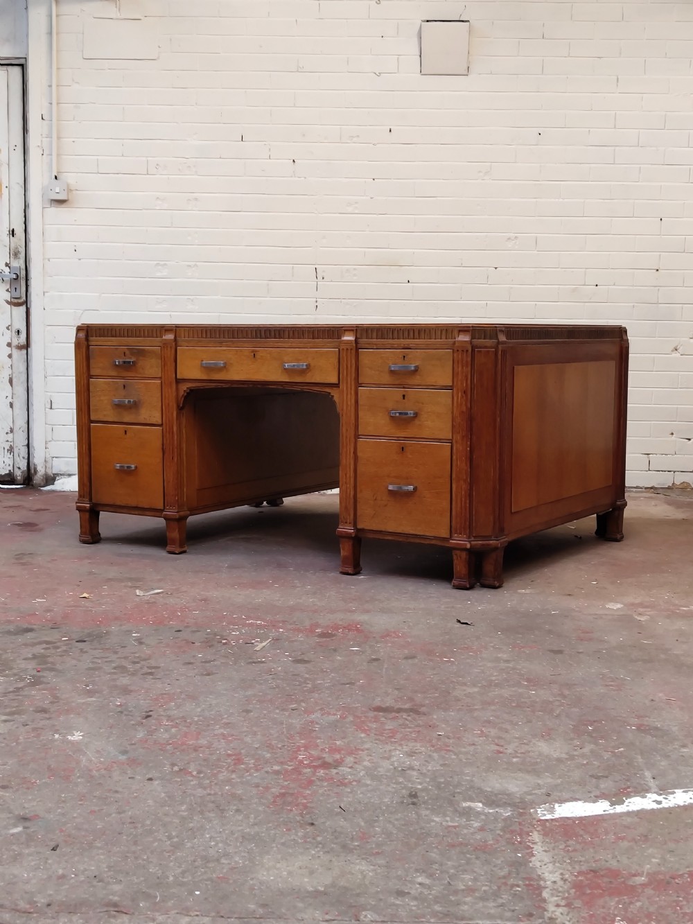 A large golden oak Art Deco partners desk featuring reeded corner details, dual pedestals with drawers, and metal pull handles. View XVIII