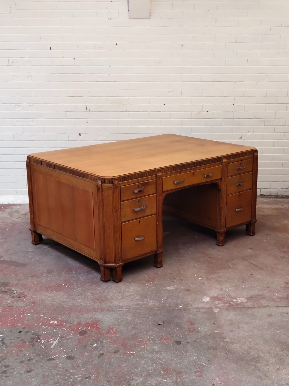 A large golden oak Art Deco partners desk featuring reeded corner details, dual pedestals with drawers, and metal pull handles. View XIX