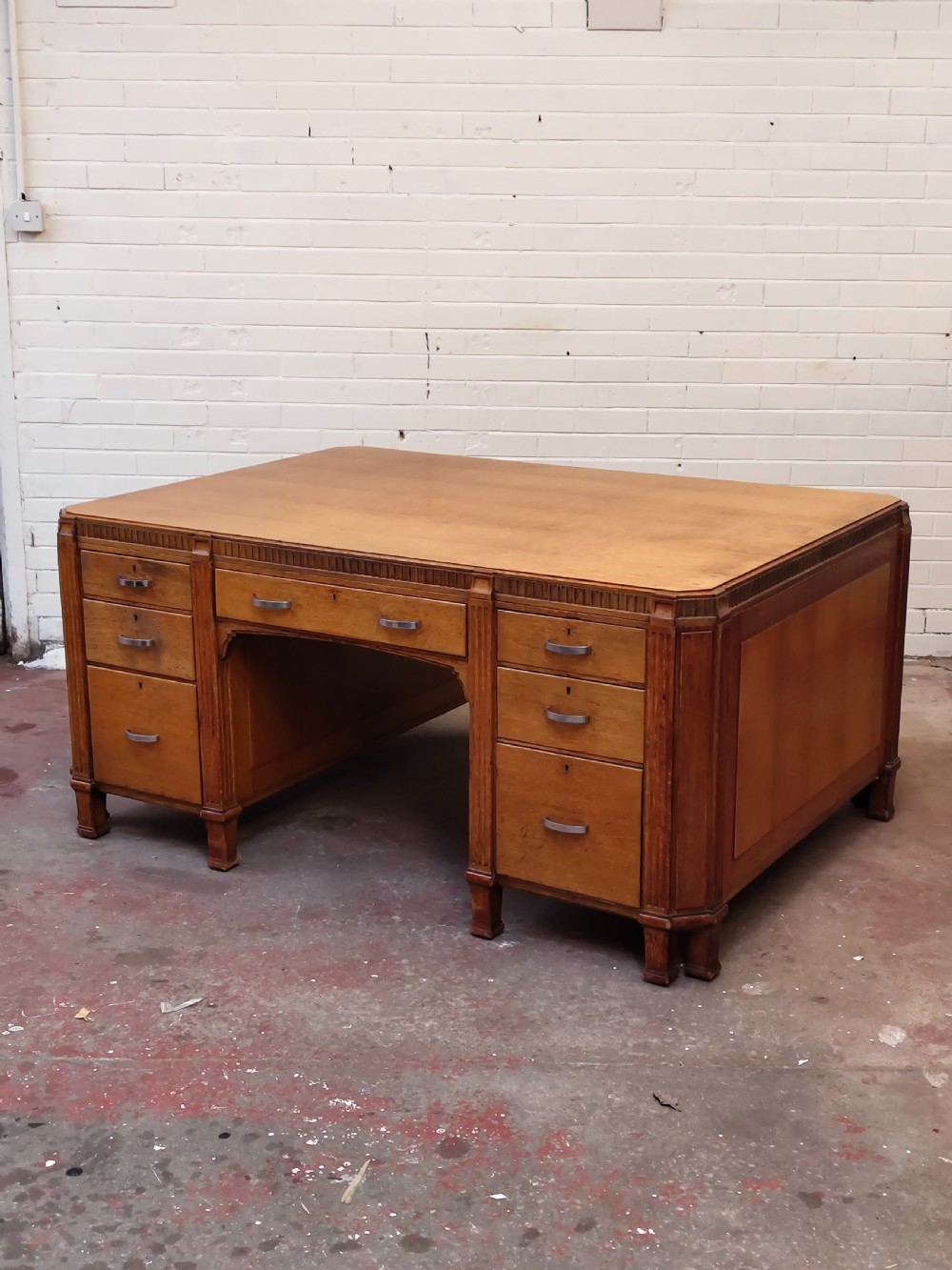A large golden oak Art Deco partners desk featuring reeded corner details, dual pedestals with drawers, and metal pull handles. View XXI