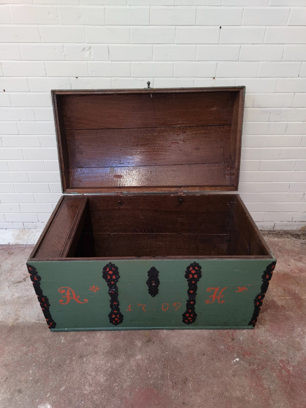 A green painted wooden dome top trunk featuring black decorative iron straps, red painted initials AH, and the date 1709. View X