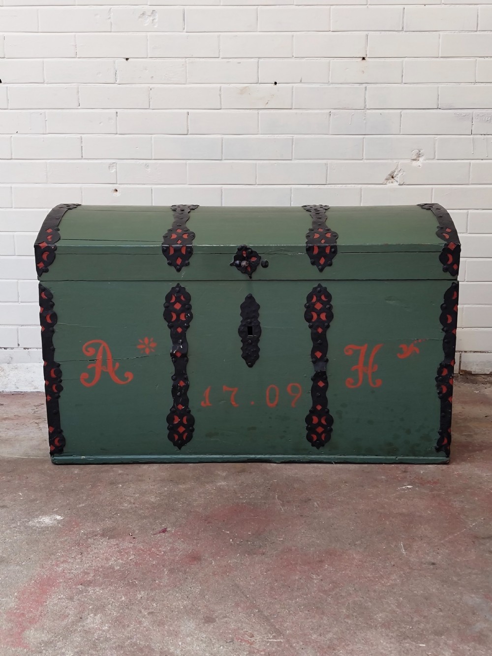 A green painted wooden dome top trunk featuring black decorative iron straps, red painted initials AH, and the date 1709. View VII