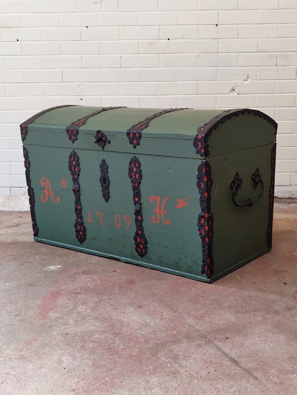 A green painted wooden dome top trunk featuring black decorative iron straps, red painted initials AH, and the date 1709.