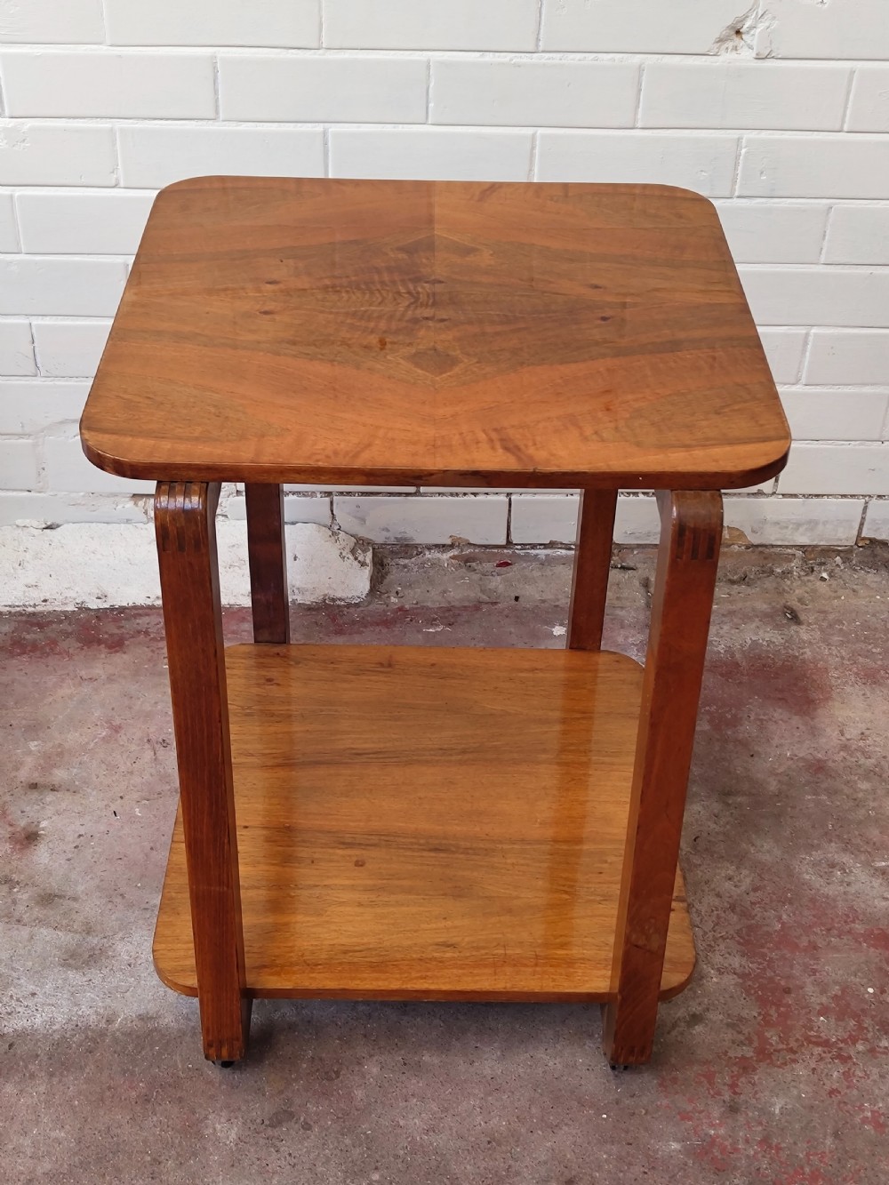 A matching pair of two-tier Art Deco burr walnut bedside tables featuring rounded tops, lower shelves, curved upright legs, and small castor wheels. View II