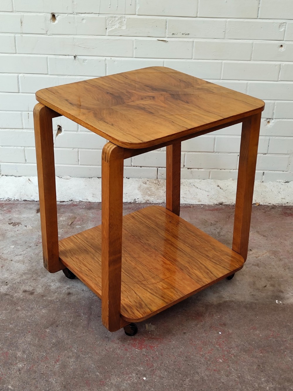 A matching pair of two-tier Art Deco burr walnut bedside tables featuring rounded tops, lower shelves, curved upright legs, and small castor wheels. View III