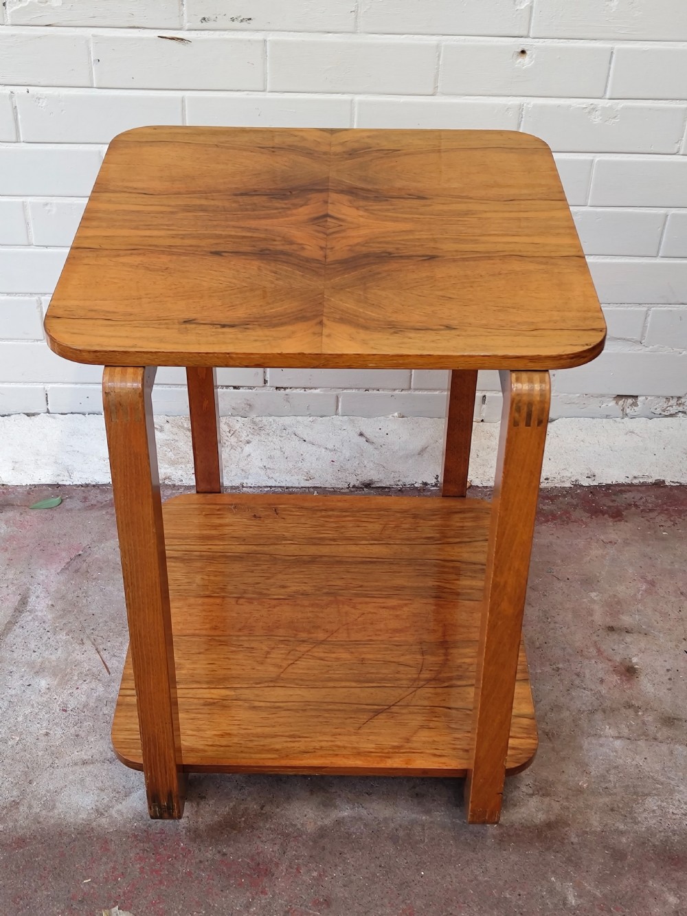 A matching pair of two-tier Art Deco burr walnut bedside tables featuring rounded tops, lower shelves, curved upright legs, and small castor wheels. View IV