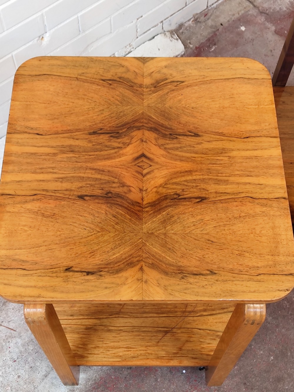 A matching pair of two-tier Art Deco burr walnut bedside tables featuring rounded tops, lower shelves, curved upright legs, and small castor wheels. View V