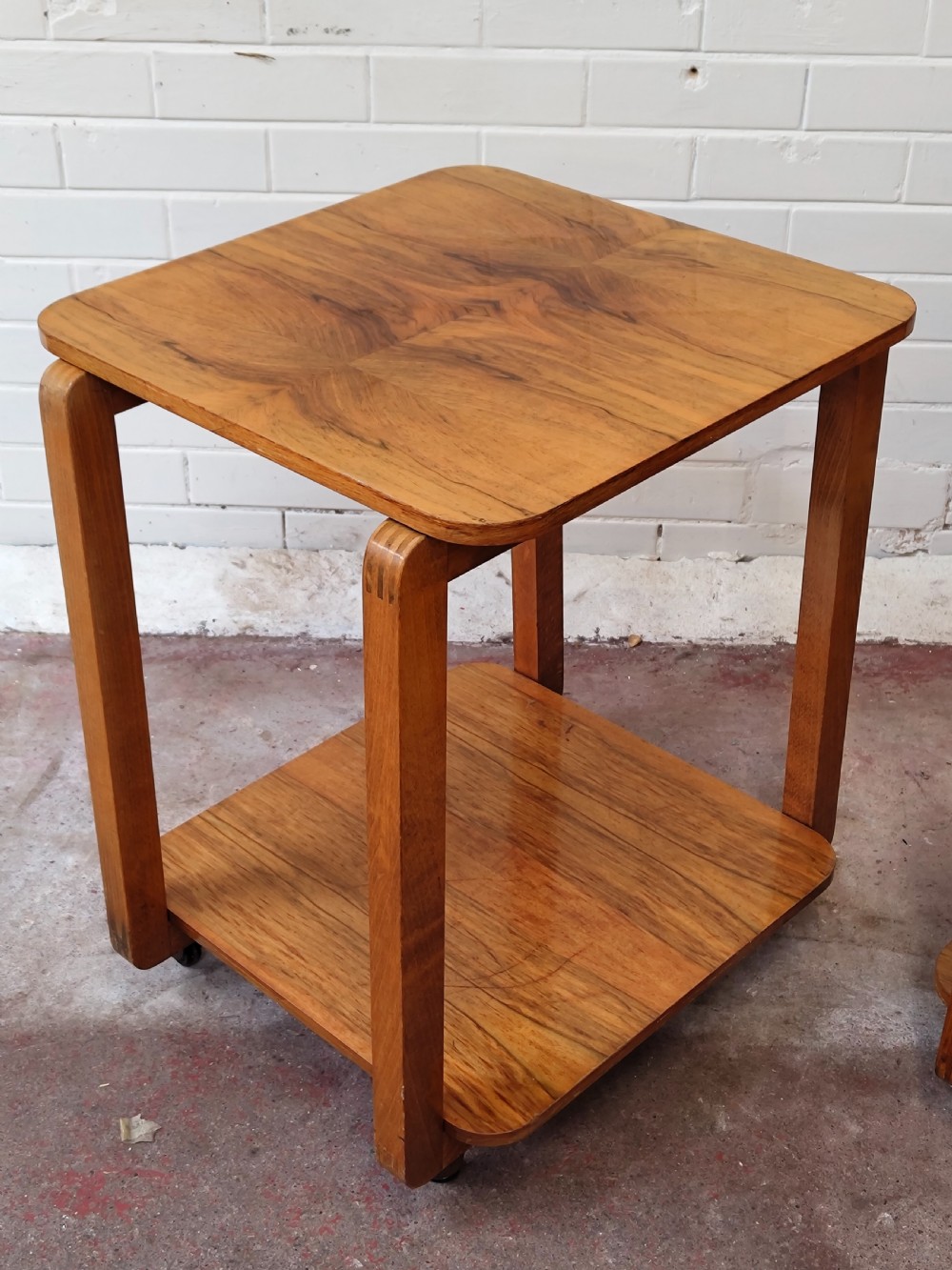 A matching pair of two-tier Art Deco burr walnut bedside tables featuring rounded tops, lower shelves, curved upright legs, and small castor wheels. View IX