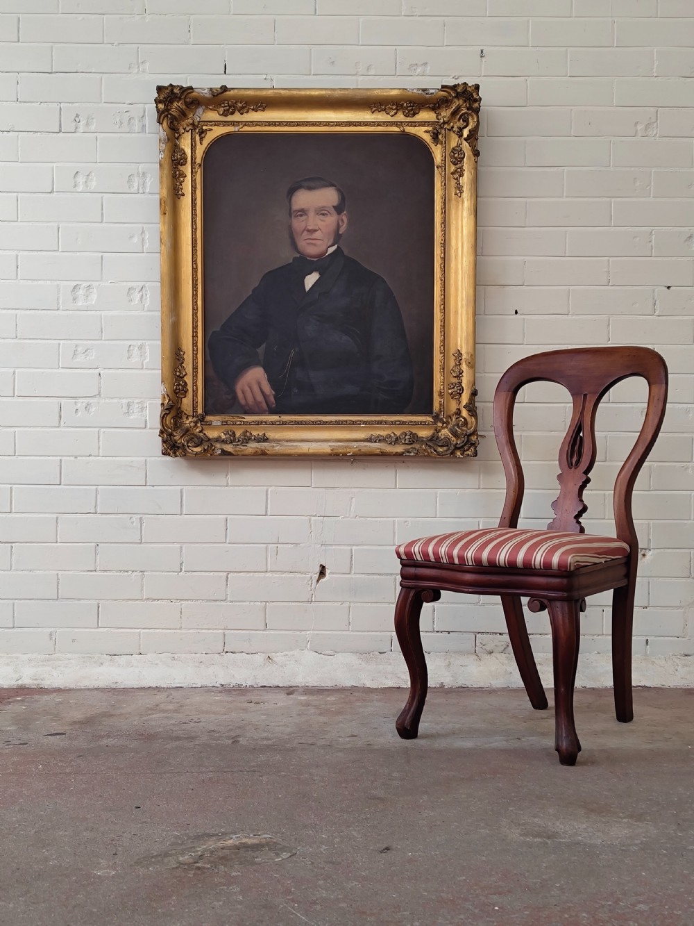 A Victorian oil painting depicting a seated gentleman in a dark suit set inside a large, ornate gilded gesso frame. View III