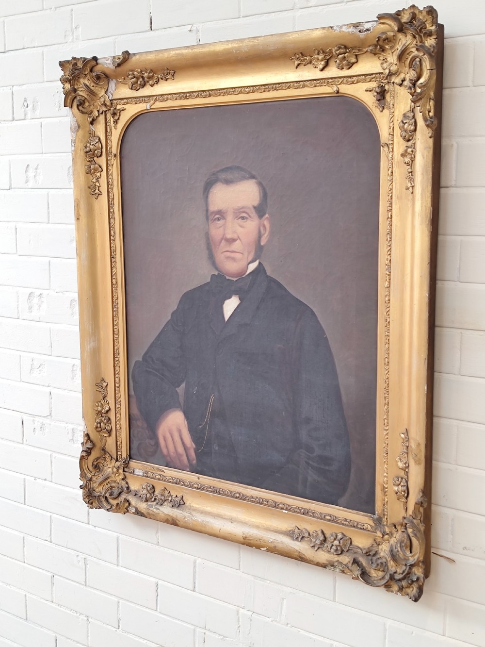 A Victorian oil painting depicting a seated gentleman in a dark suit set inside a large, ornate gilded gesso frame. View XIII