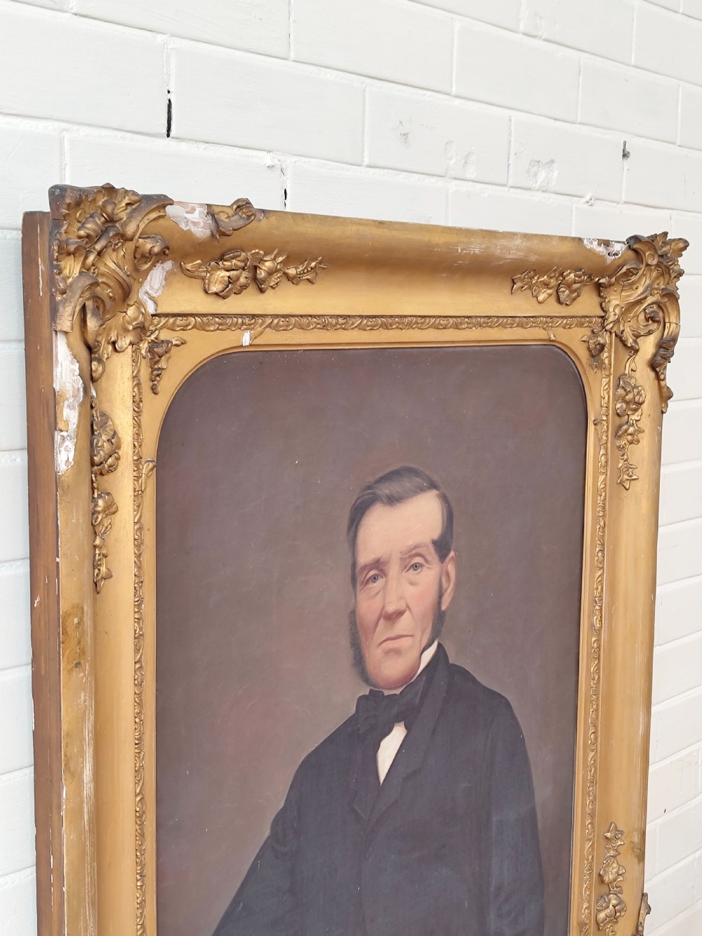 A Victorian oil painting depicting a seated gentleman in a dark suit set inside a large, ornate gilded gesso frame. View XIV
