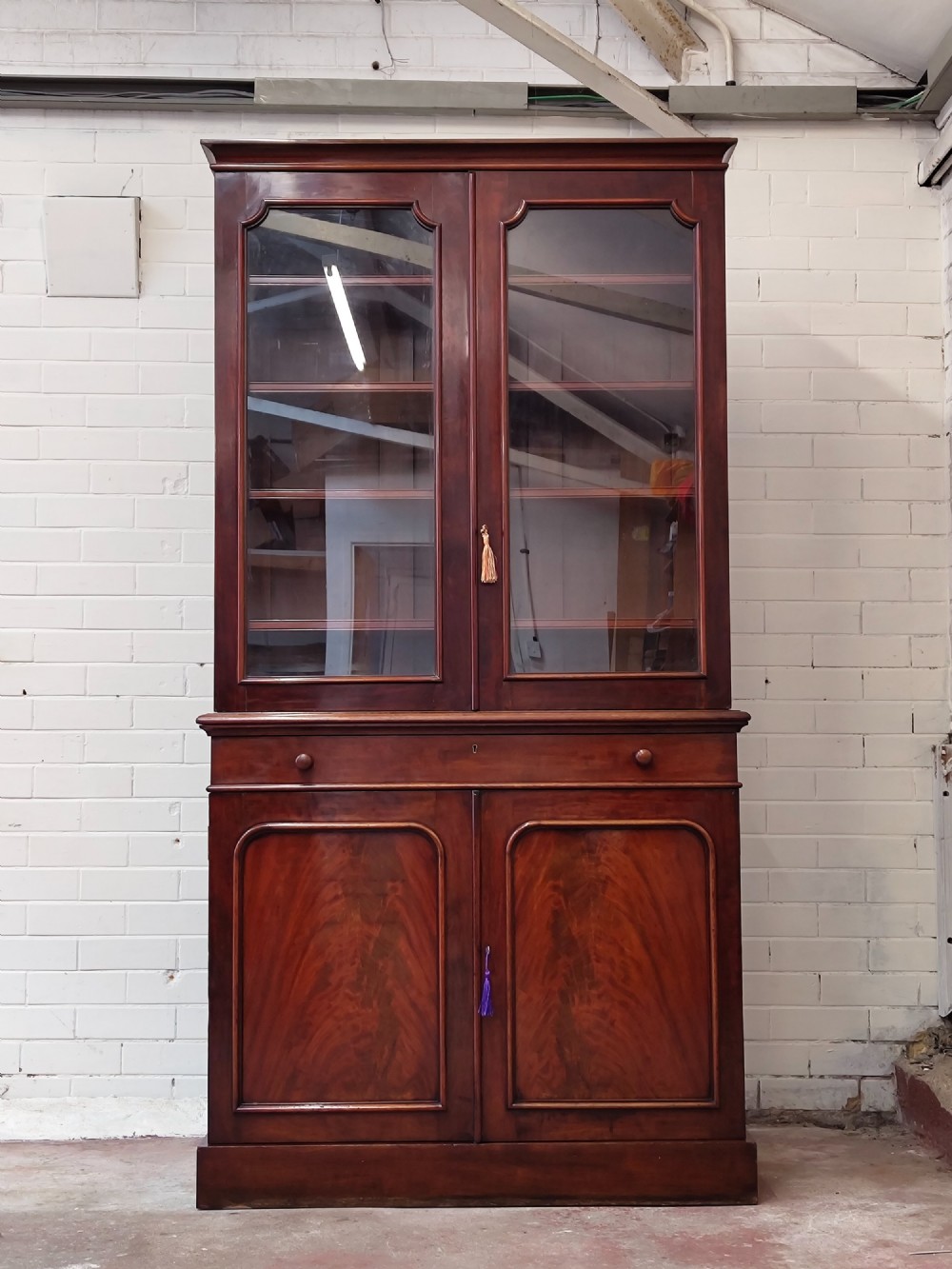 A tall Victorian mahogany bookcase featuring a glazed upper display cabinet with adjustable shelves over a lower two-door cupboard with flame mahogany veneer panels.