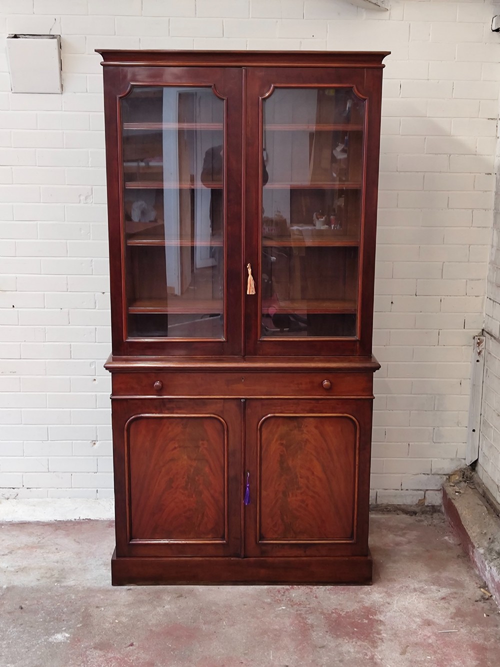 A tall Victorian mahogany bookcase featuring a glazed upper display cabinet with adjustable shelves over a lower two-door cupboard with flame mahogany veneer panels. View II