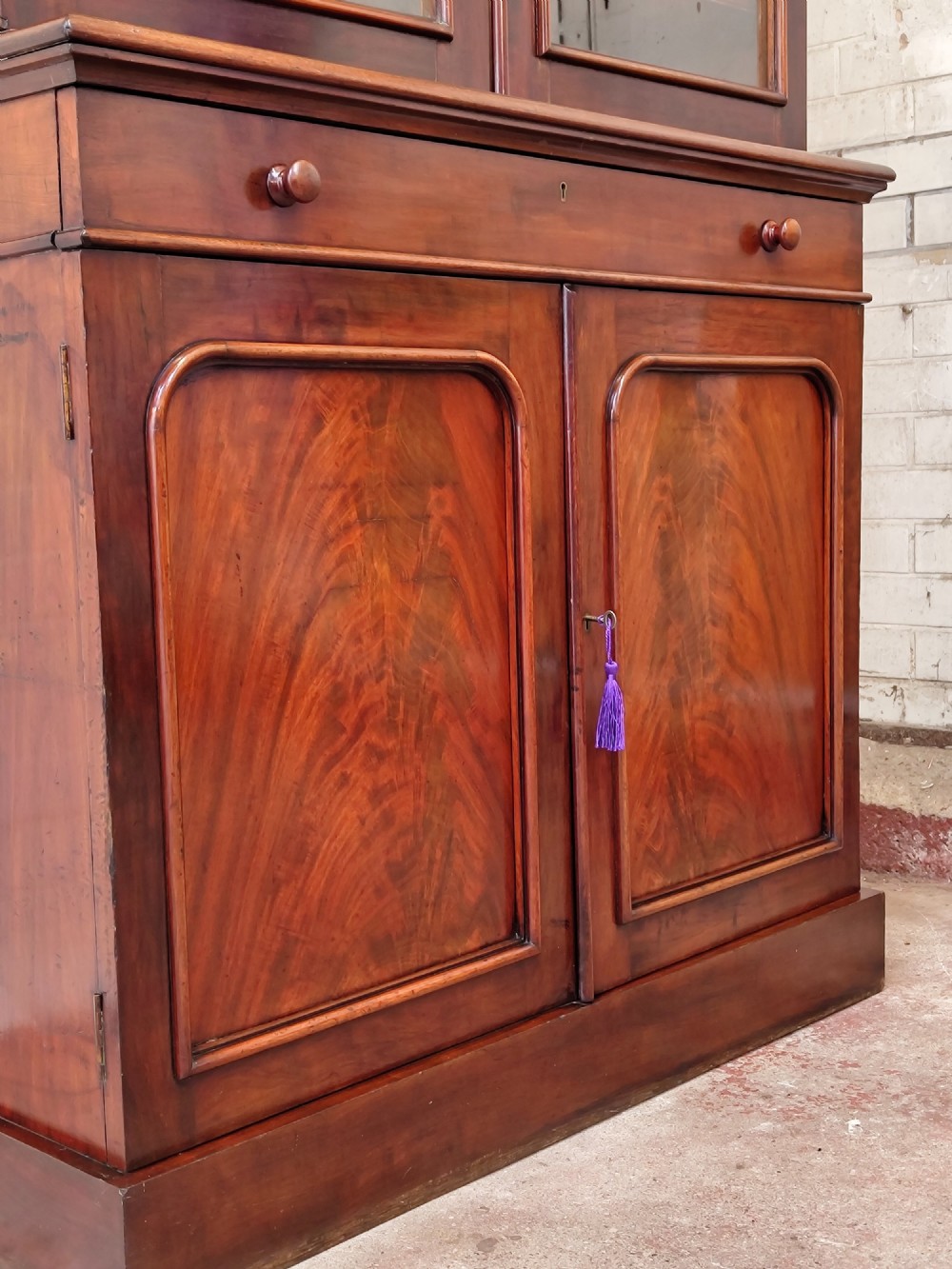 A tall Victorian mahogany bookcase featuring a glazed upper display cabinet with adjustable shelves over a lower two-door cupboard with flame mahogany veneer panels. View V