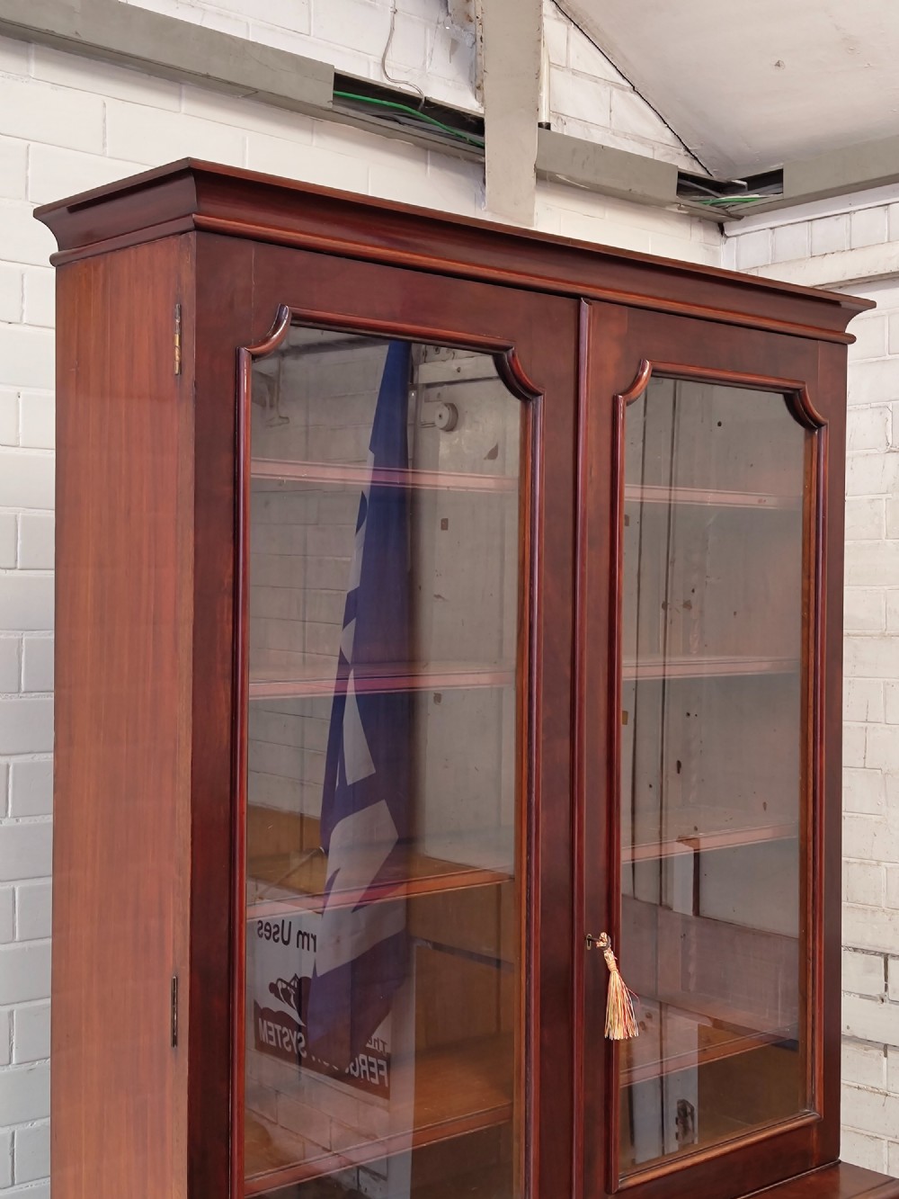 A tall Victorian mahogany bookcase featuring a glazed upper display cabinet with adjustable shelves over a lower two-door cupboard with flame mahogany veneer panels. View VII