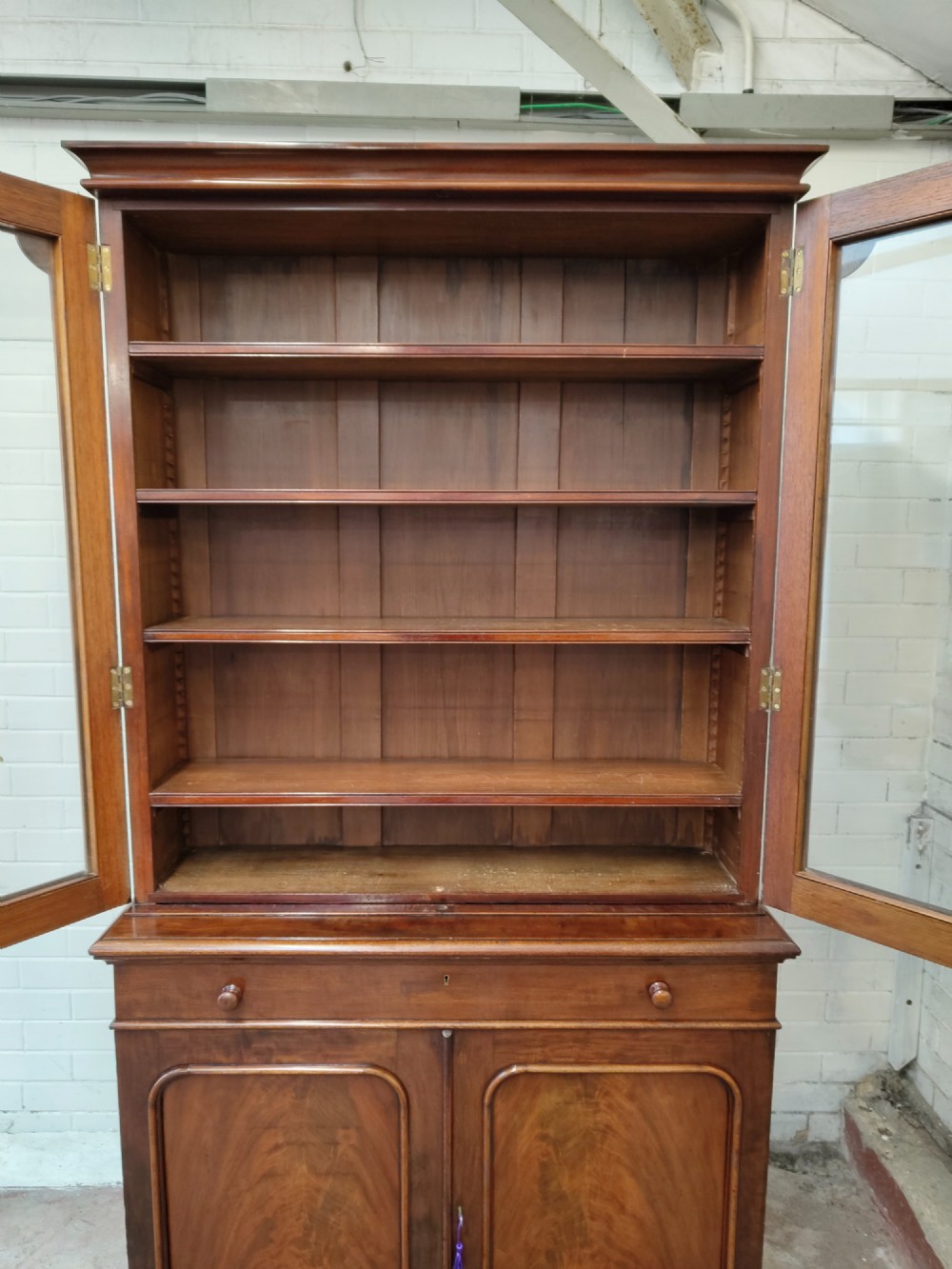 A tall Victorian mahogany bookcase featuring a glazed upper display cabinet with adjustable shelves over a lower two-door cupboard with flame mahogany veneer panels. View VIII
