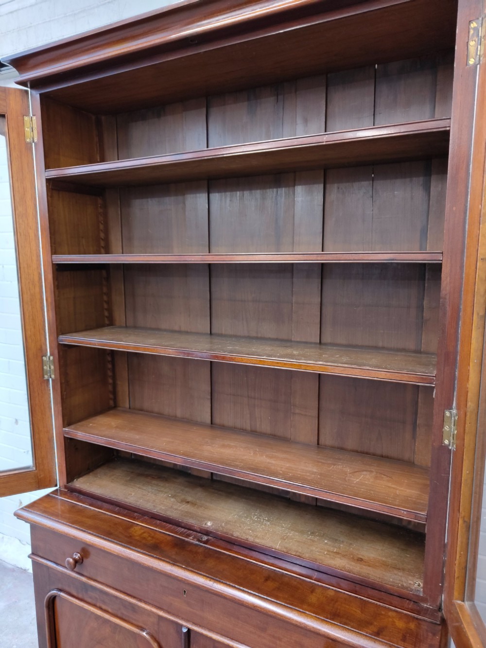 A tall Victorian mahogany bookcase featuring a glazed upper display cabinet with adjustable shelves over a lower two-door cupboard with flame mahogany veneer panels. View IX