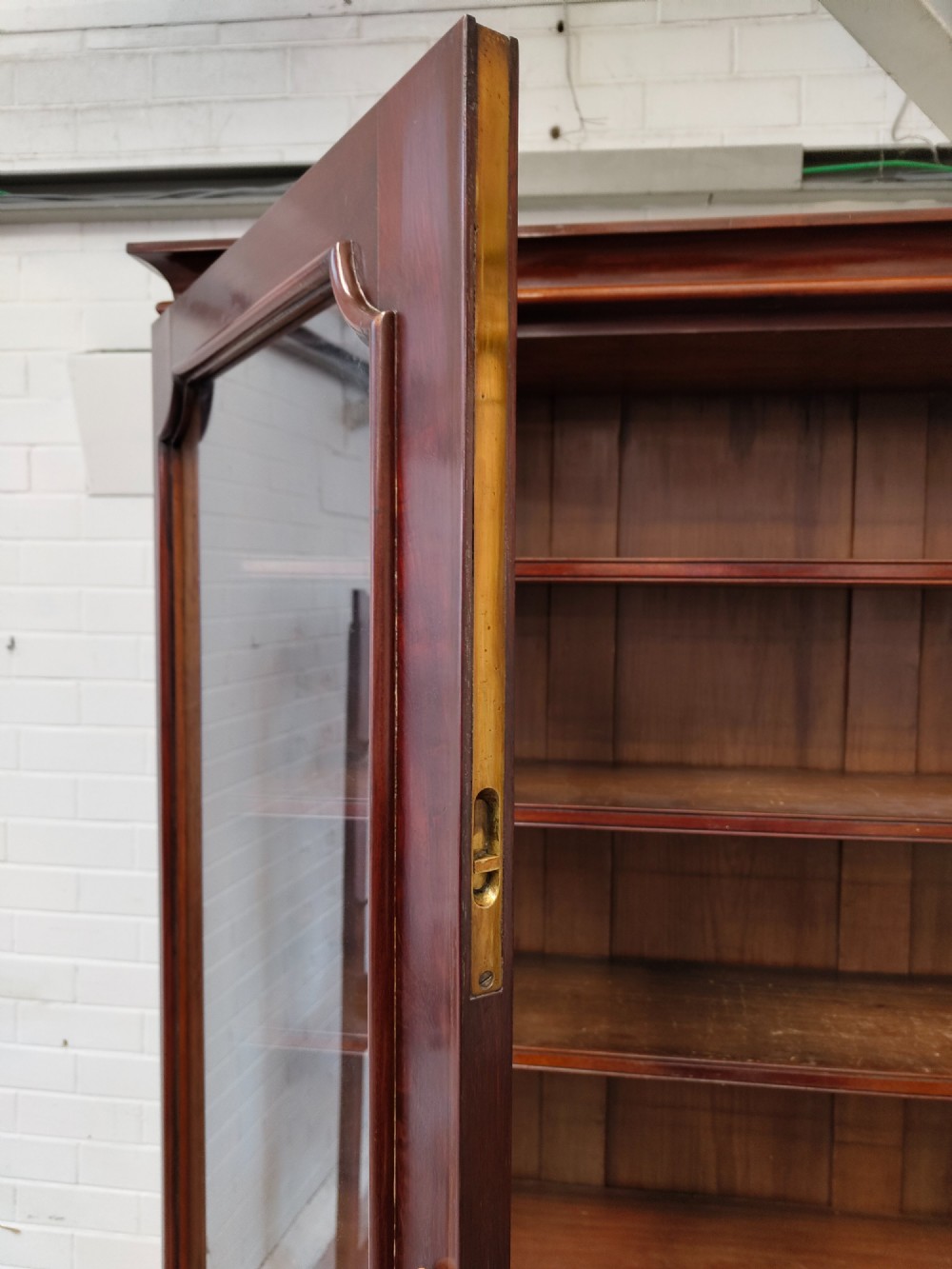 A tall Victorian mahogany bookcase featuring a glazed upper display cabinet with adjustable shelves over a lower two-door cupboard with flame mahogany veneer panels. View X