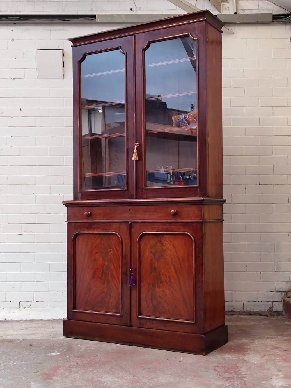 A tall Victorian mahogany bookcase featuring a glazed upper display cabinet with adjustable shelves over a lower two-door cupboard with flame mahogany veneer panels. View XIV