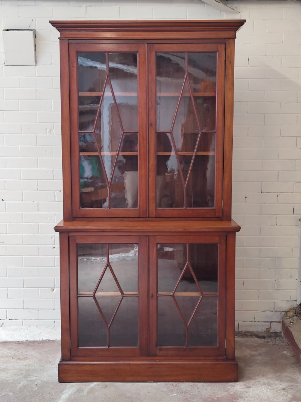 A tall Victorian mahogany bookcase featuring upper and lower double doors with diamond astragal glazed panels and adjustable interior shelves.