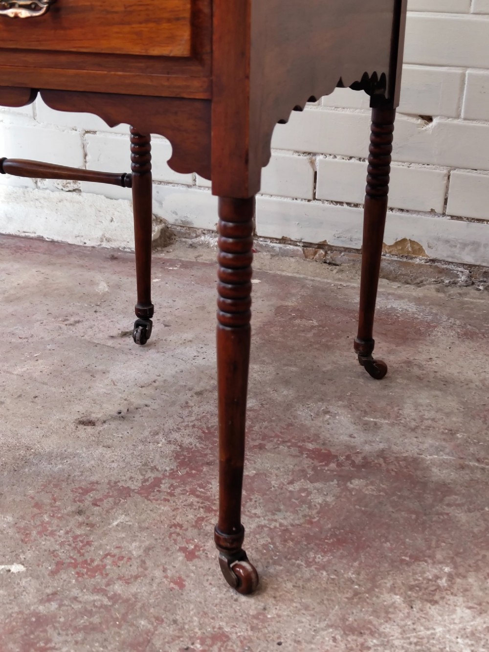 An Edwardian mahogany ladies writing desk featuring a green leather writing surface, an asymmetric upper cabinet with gallery shelving, multiple drawers with brass handles, and slender turned legs on castors. View III