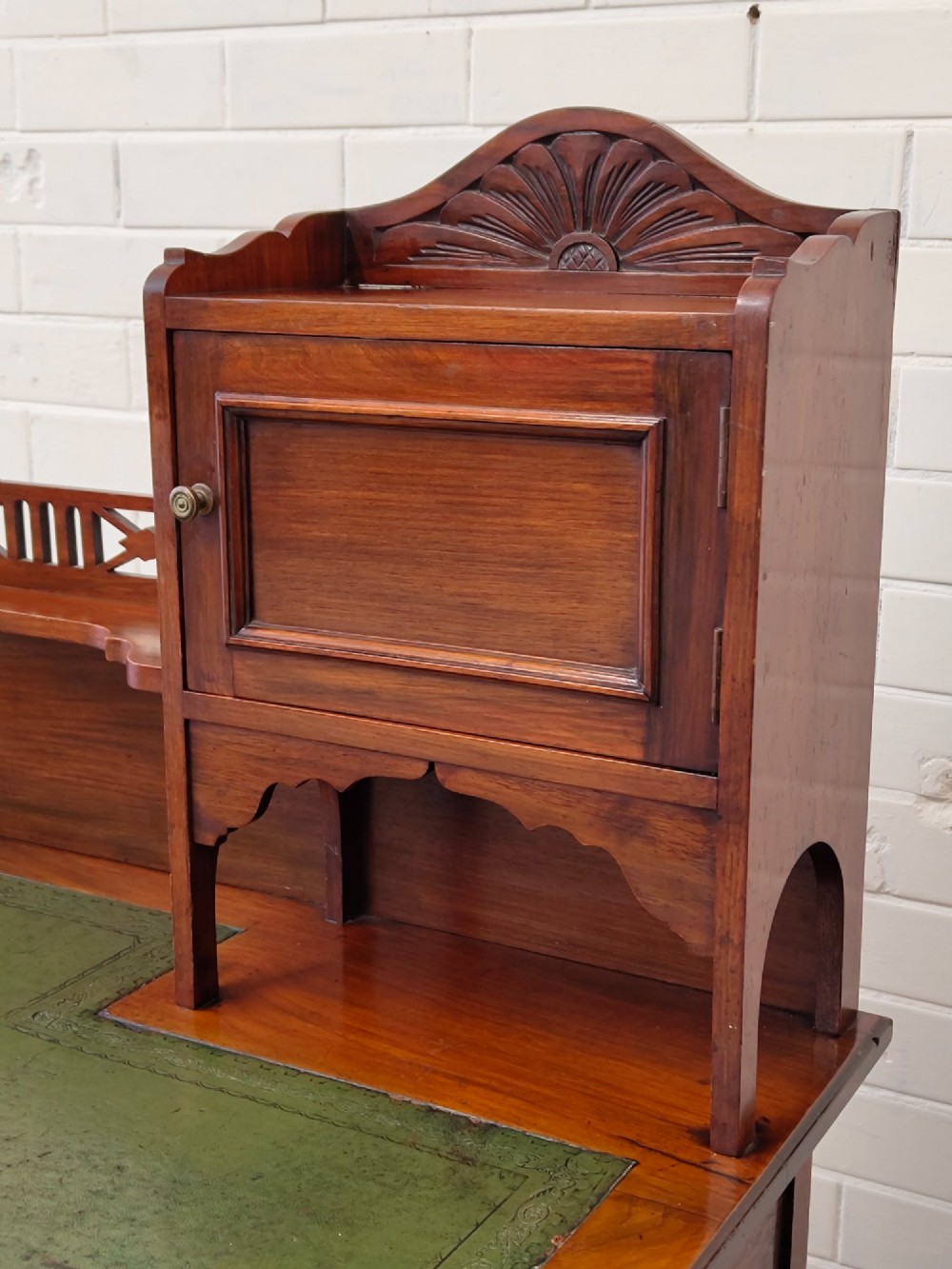 An Edwardian mahogany ladies writing desk featuring a green leather writing surface, an asymmetric upper cabinet with gallery shelving, multiple drawers with brass handles, and slender turned legs on castors. View V