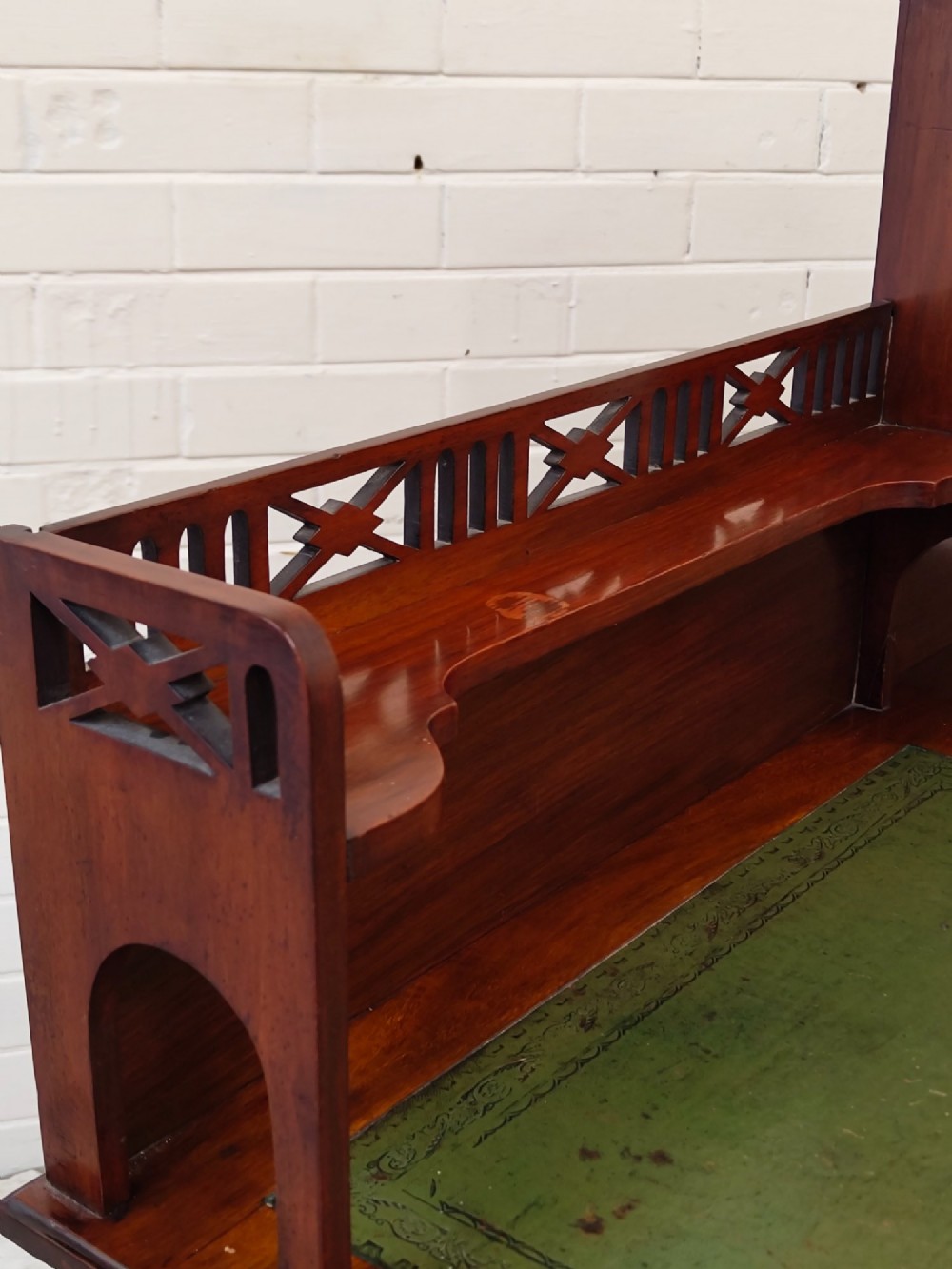 An Edwardian mahogany ladies writing desk featuring a green leather writing surface, an asymmetric upper cabinet with gallery shelving, multiple drawers with brass handles, and slender turned legs on castors. View XI