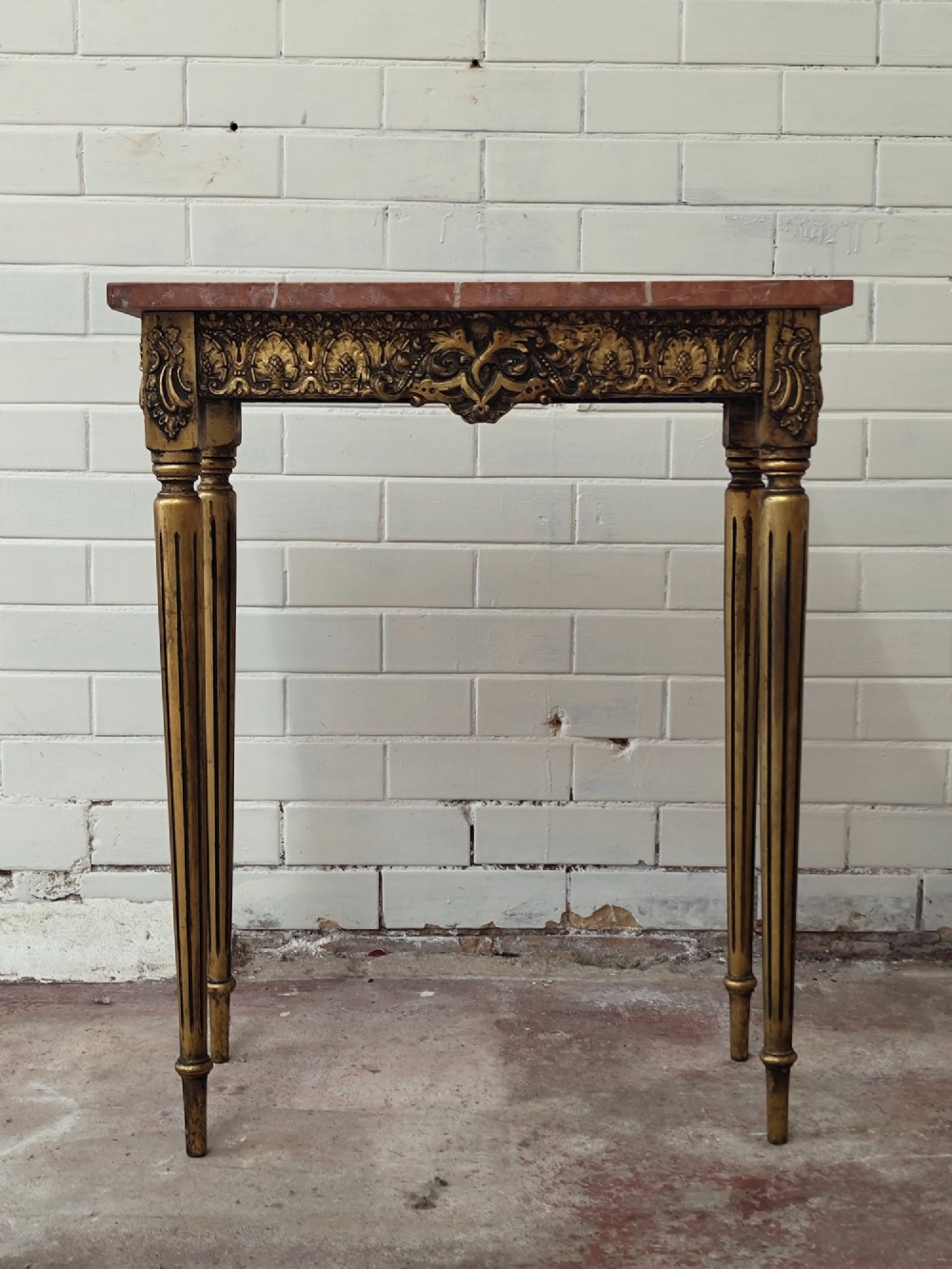 A diminutive French Louis XVI style giltwood console table with a red veined marble top, carved frieze, and slender tapered fluted legs. View II