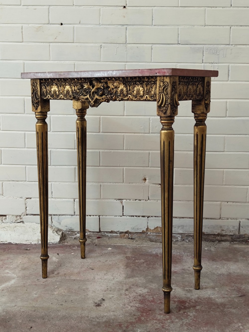 A diminutive French Louis XVI style giltwood console table with a red veined marble top, carved frieze, and slender tapered fluted legs. View XIV