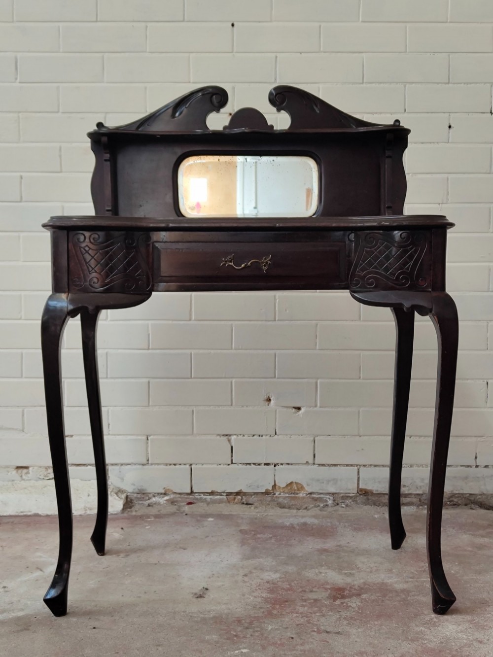 A dark mahogany Victorian ladies writing desk featuring slender cabriole legs, a single drawer, carved lattice details, and a raised back structure with a small central mirror.
